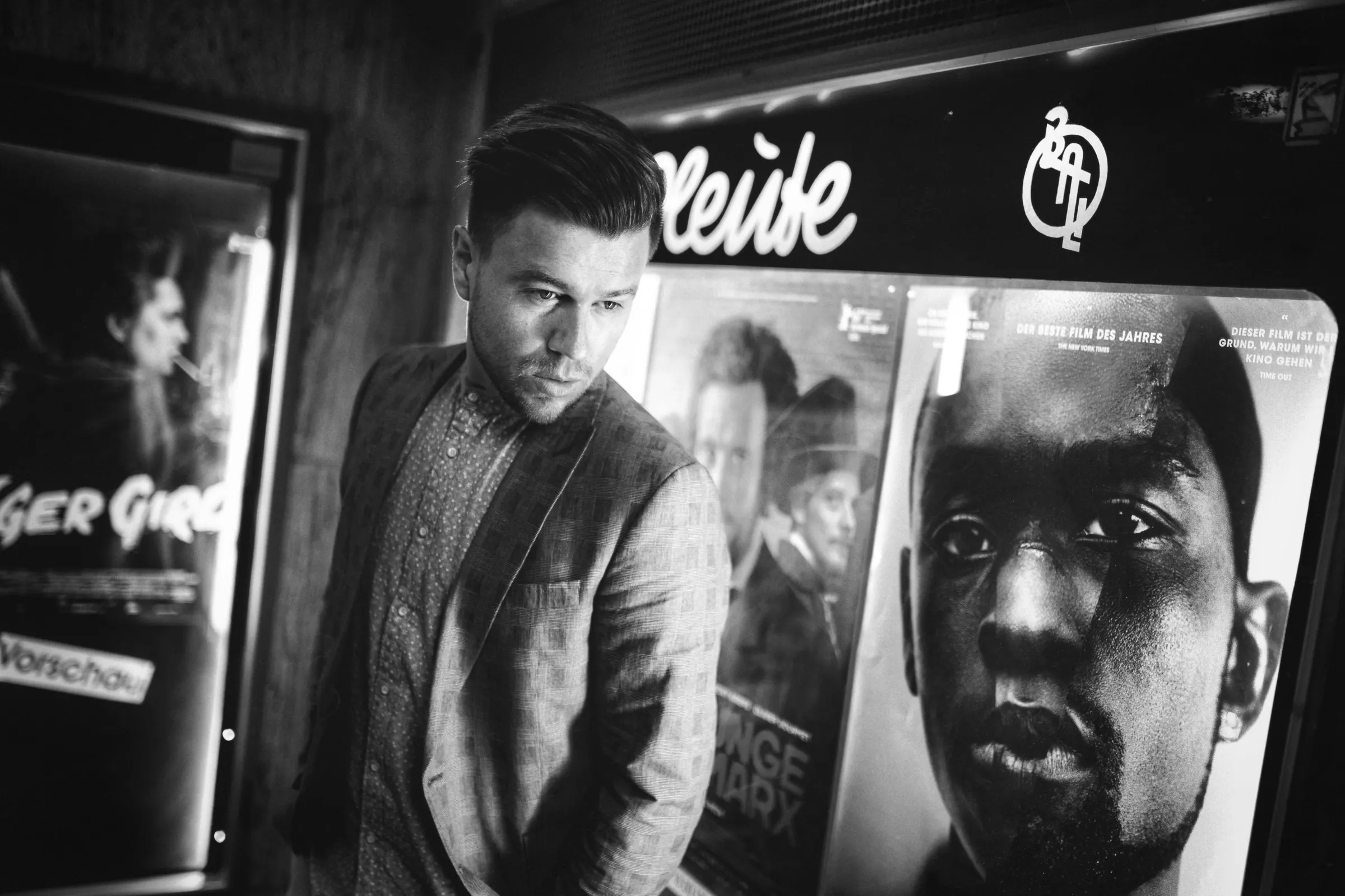Schwarzweiß-Editorial: Mann im Kinofoyer zwischen Filmplakaten