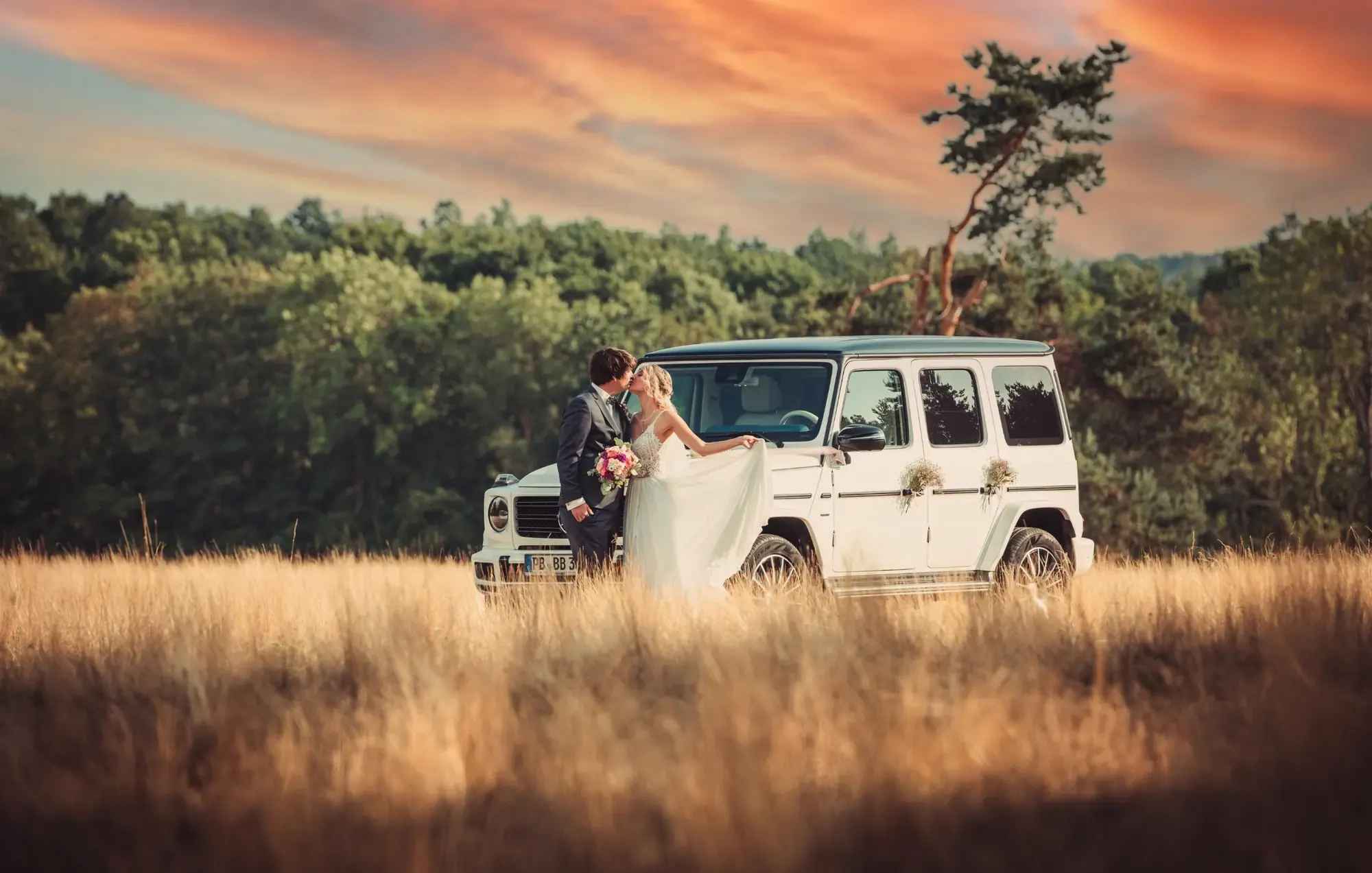 Hochzeitsfotografie: Brautpaar küsst sich vor einem weißen Geländewagen im Sonnenuntergang