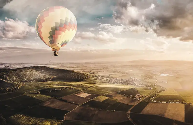 Luftaufnahme: Heißluftballon über weiter Landschaft im Abendlicht