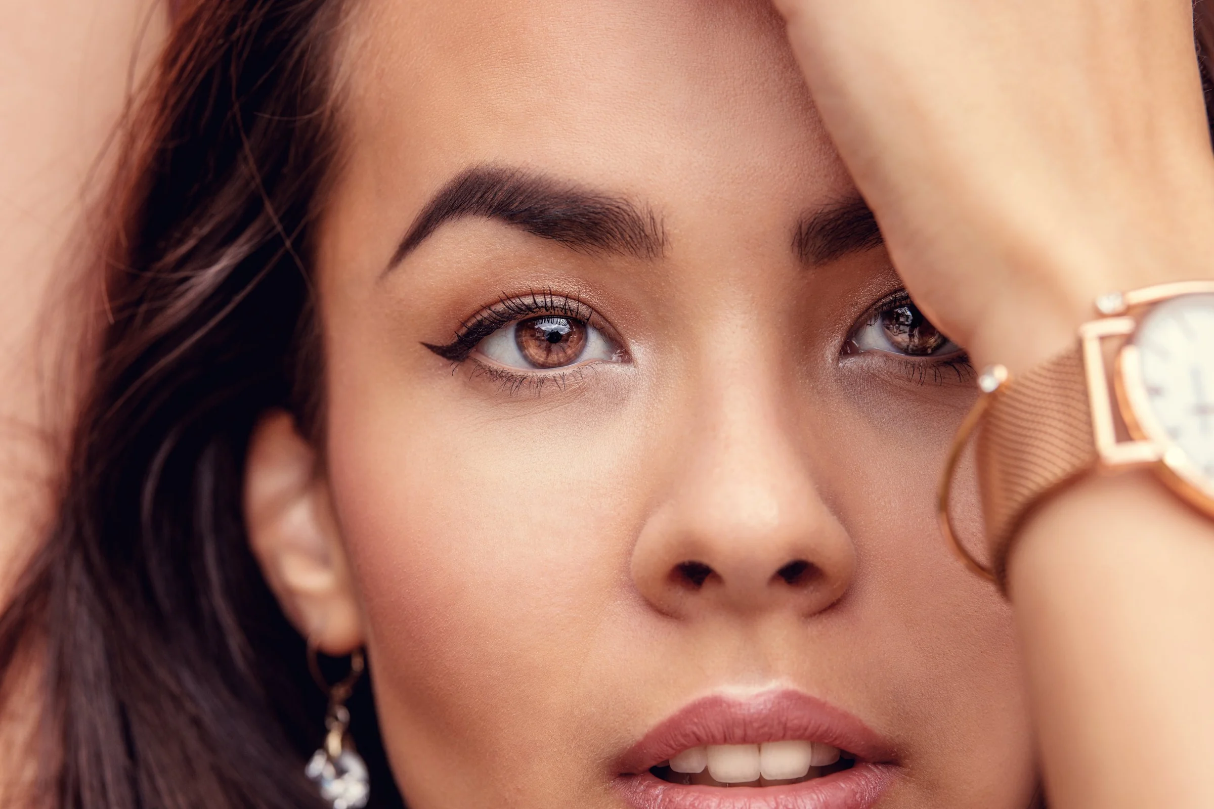 Beauty-Porträt einer Frau mit braunen Augen, Lidstrich und Armbanduhr, die Hand im Haar