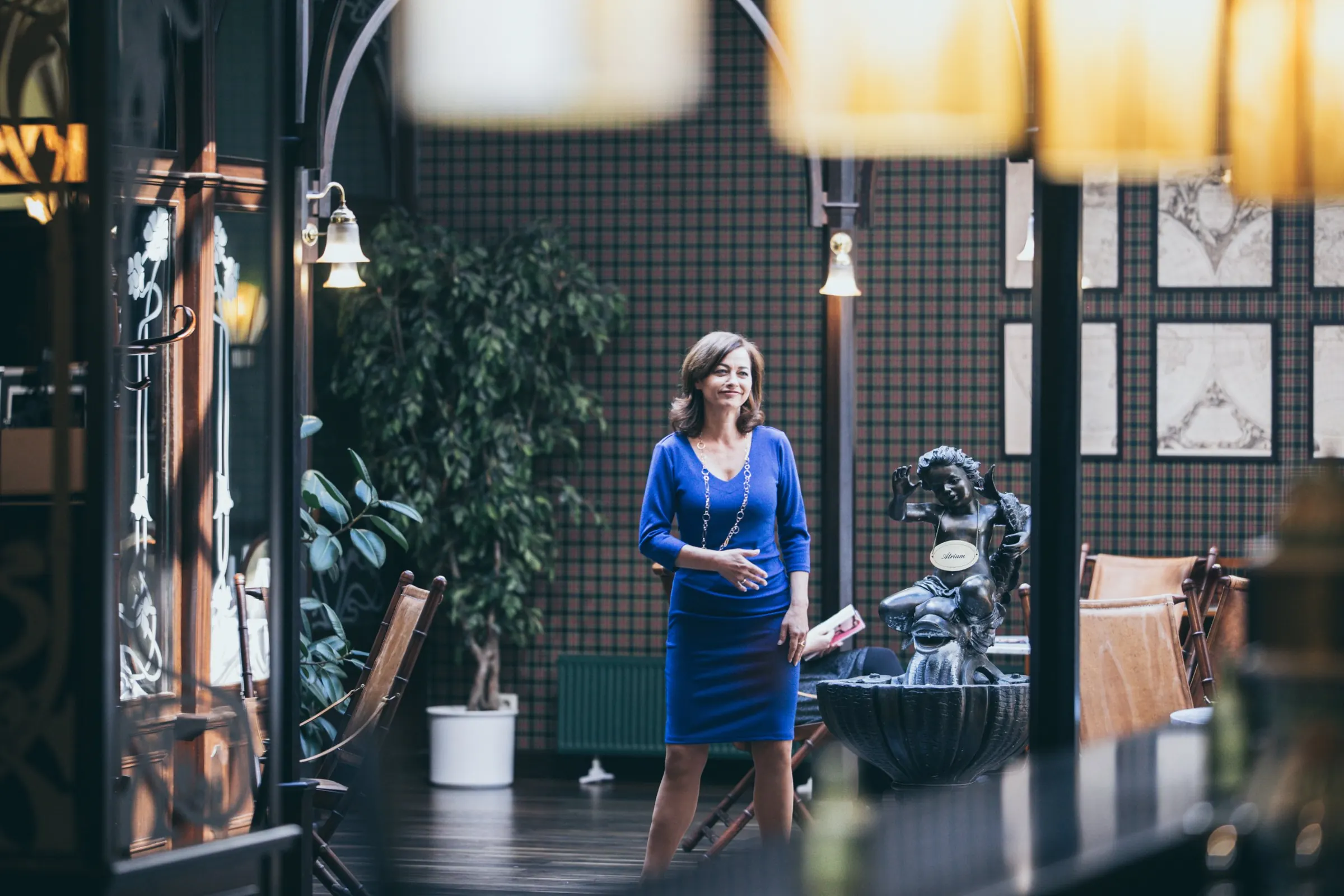 Standfotografie am Set: Darstellerin im blauen Kleid in einem Atrium mit karierter Tapete