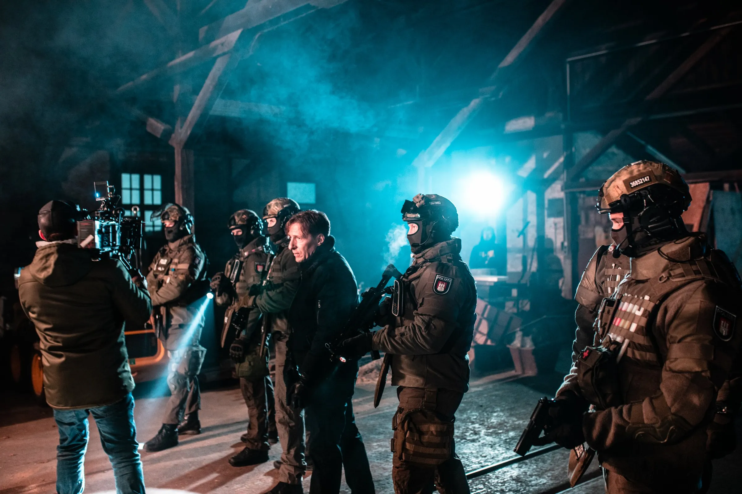 Setfoto aus der Teaserproduktion „WORN“: Darsteller in Einsatzkleidung bei einem Nachtdreh in einer Halle, links die Kamera